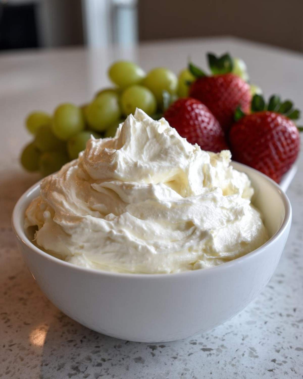 A bowl of fluffy white fruit dip served alongside fresh strawberries and green grapes.