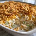 A scoop has been taken out of a creamy hot chicken salad casserole topped with melted cheese and crunchy cornflakes.