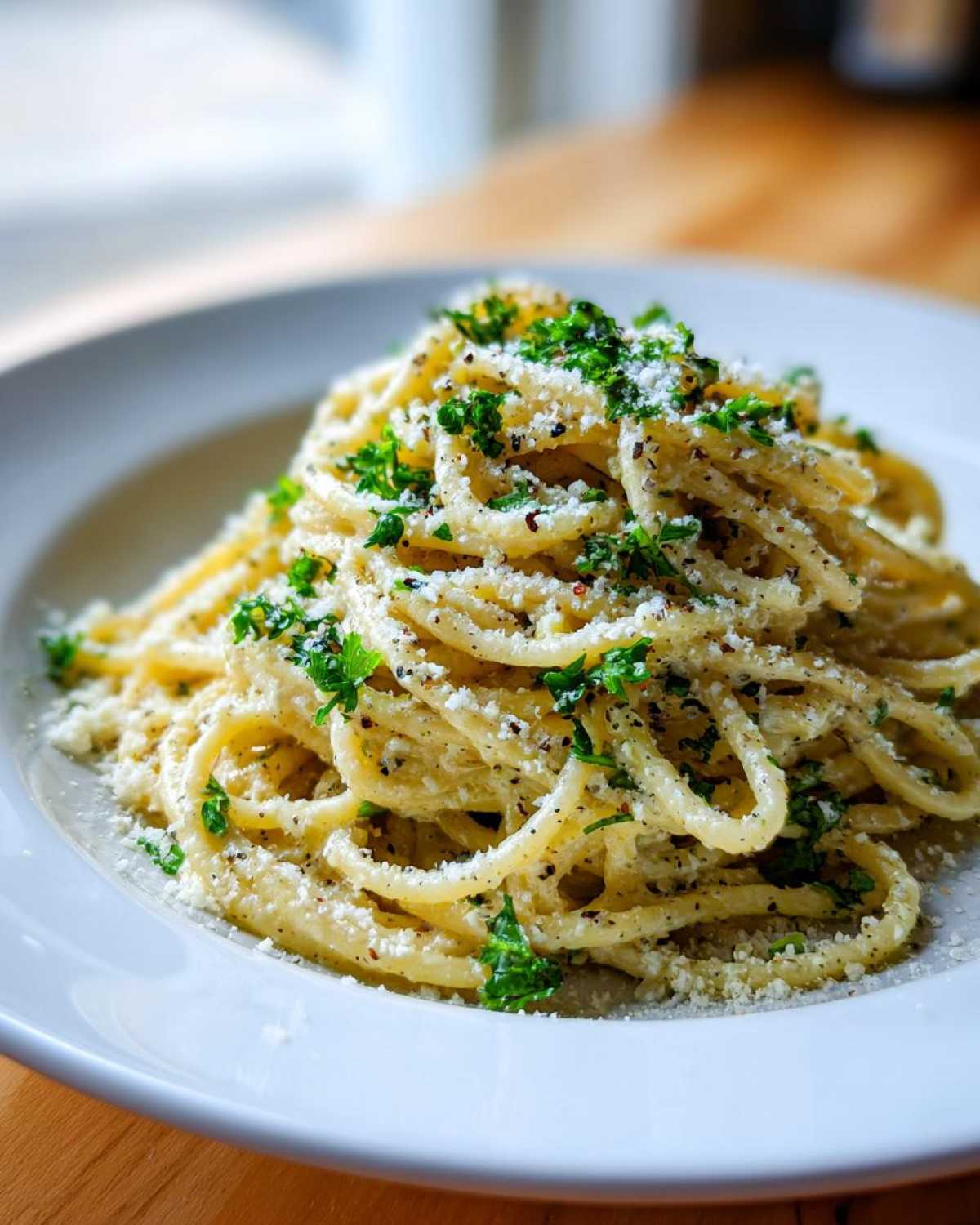 A close-up shot of creamy parmesan pasta tossed with black pepper and topped generously with grated cheese and fresh parsley.