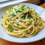 A close-up serving of creamy parmesan pasta, topped generously with grated cheese, black pepper, and fresh chopped parsley.
