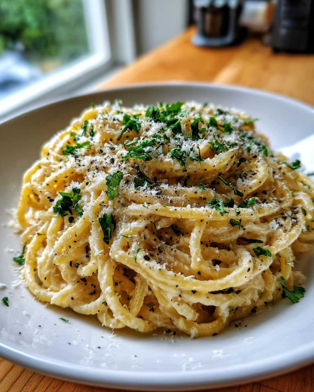 Close-up of a serving of creamy parmesan pasta, generously topped with grated cheese, black pepper, and fresh parsley.
