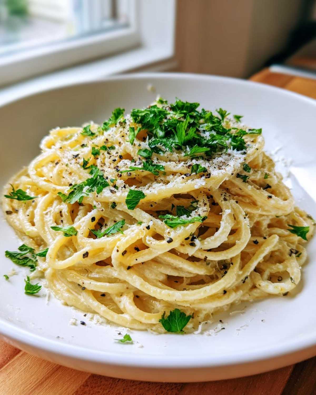 Close-up of creamy parmesan pasta tossed in sauce, topped generously with fresh parsley and cracked black pepper.