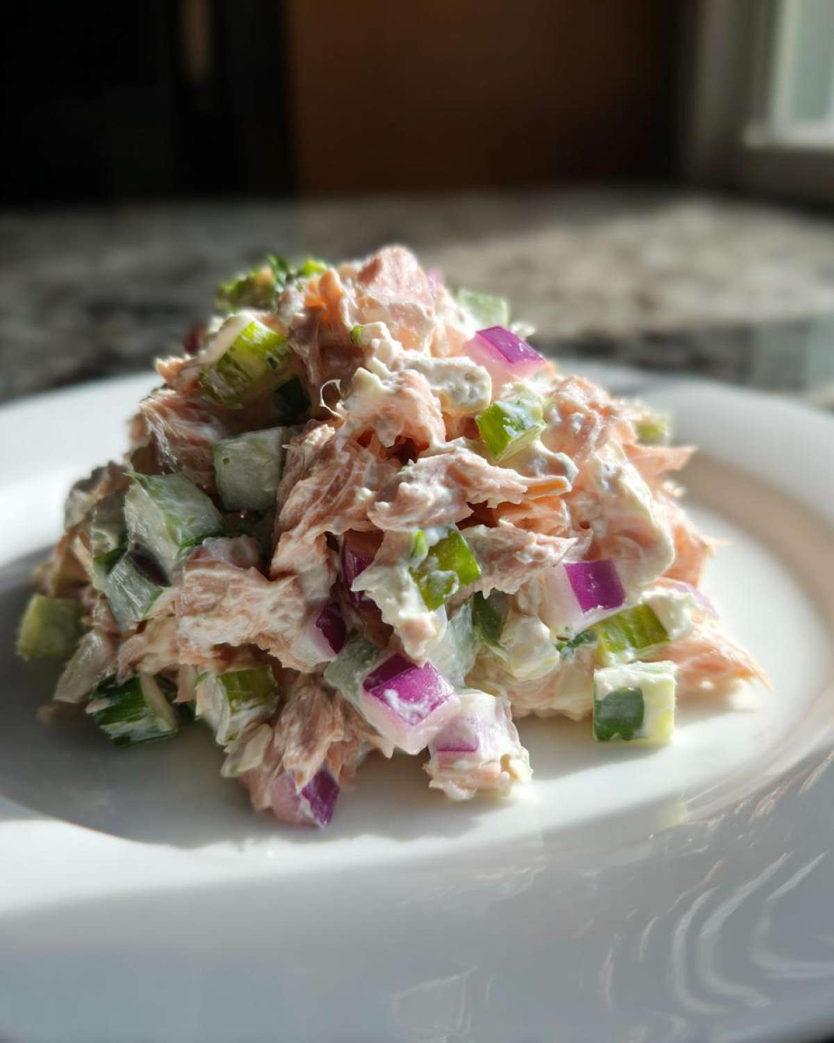 A mound of creamy salmon salad mixed with diced red onion and celery served on a white plate.