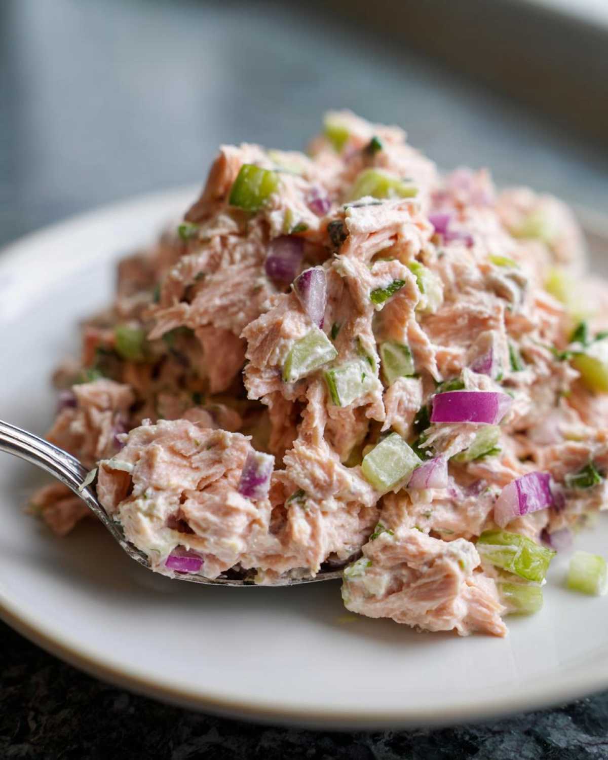 A spoonful of creamy salmon salad mixed with diced red onion and celery, ready to eat.