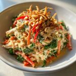 A bowl of creamy thai chicken salad mixed with shredded chicken, spinach, red peppers, and topped with peanuts and crispy fried onions.