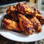A close-up of a pile of golden brown, crispy chicken wing pieces served on a white plate.