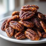 Close-up of a mound of glistening, candied cinnamon sugar pecans piled high on a white plate.