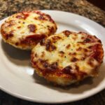 Close-up of two perfectly melted and slightly browned english muffin pizza halves on a white plate.