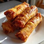Close-up of four perfectly golden brown, crispy fried egg roll appetizers stacked on a white plate.