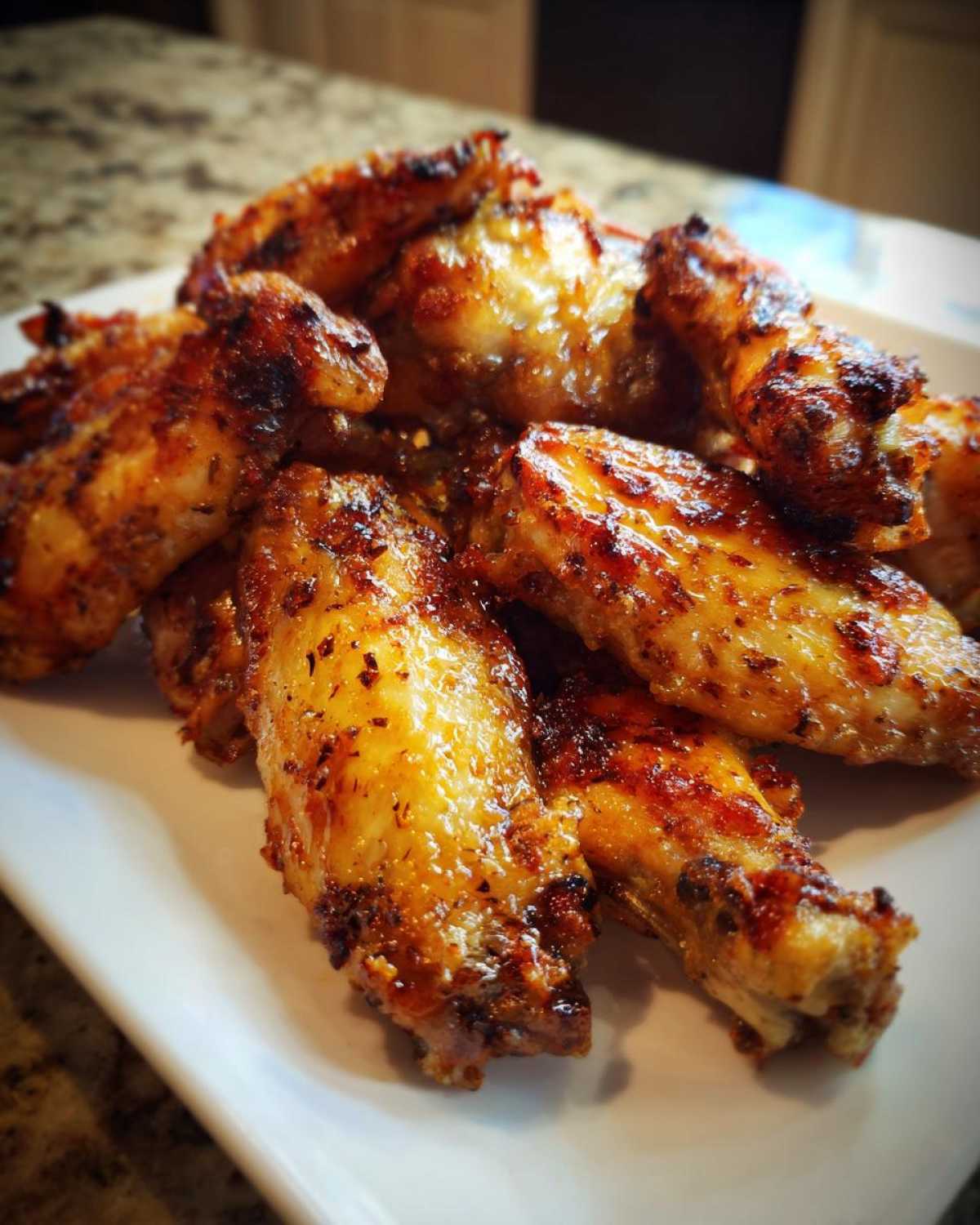 Close-up of perfectly cooked, crispy, and glazed chicken wing pieces piled high on a white serving dish.