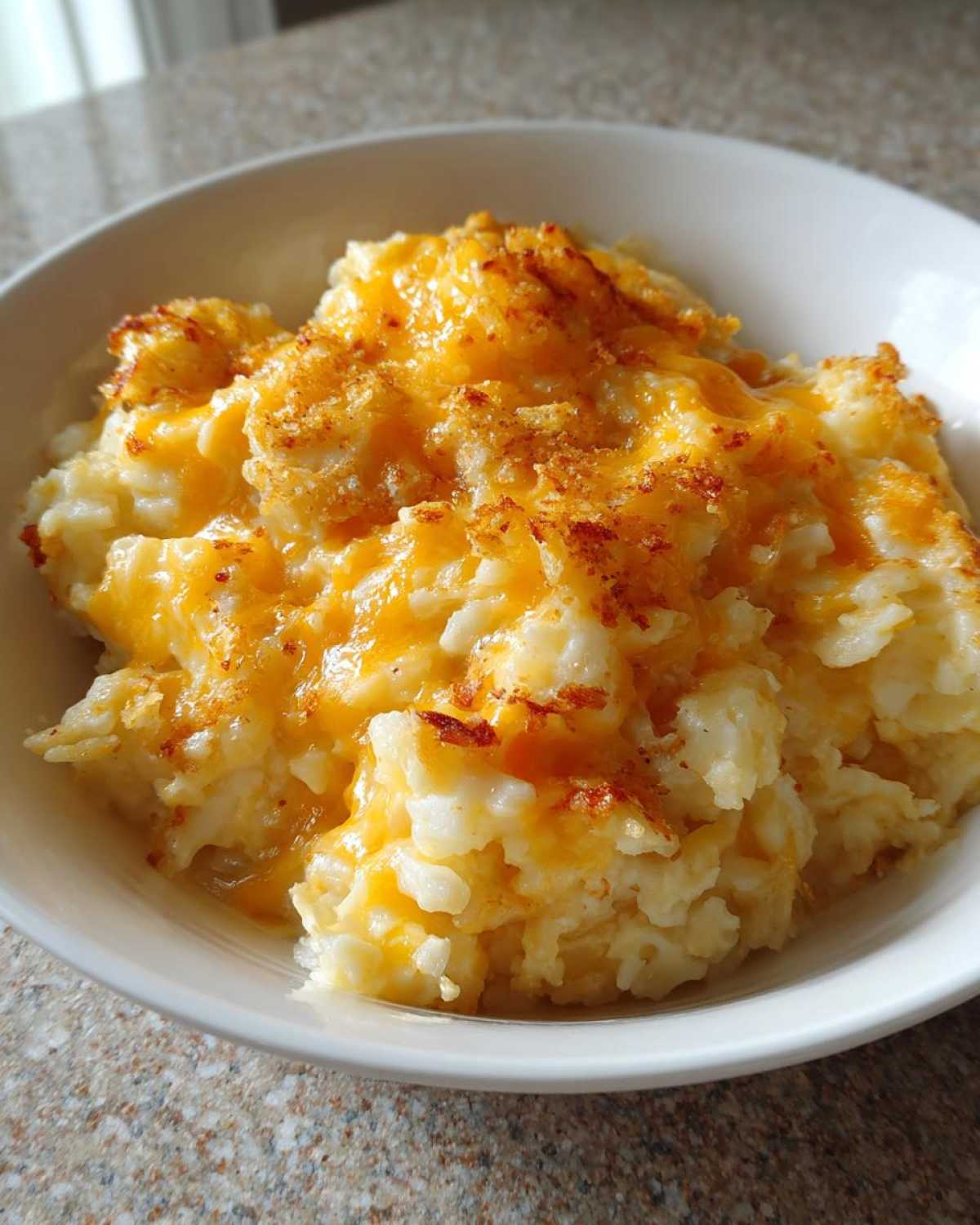 Close-up of creamy crockpot cheesy potatoes topped with melted cheddar cheese and crispy breadcrumbs.