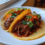 Close-up of two delicious Crockpot Korean Beef Tacos filled with saucy shredded beef, kimchi slaw, and cilantro.