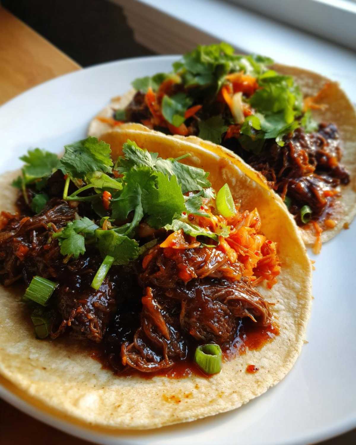 Two soft corn tortillas filled with saucy Crockpot Korean Beef Tacos, topped with shredded carrots and fresh cilantro.