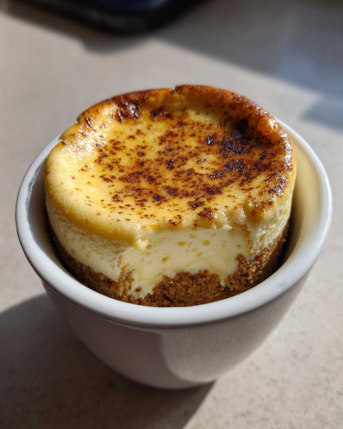 A single serving of Decadent Cheesecake Mug Recipe with a caramelized top, served in a white mug.