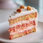 A perfect slice of Decadent Hawaiian Guava Cake showing layers of yellow cake, pink guava filling, and white frosting, topped with nuts.