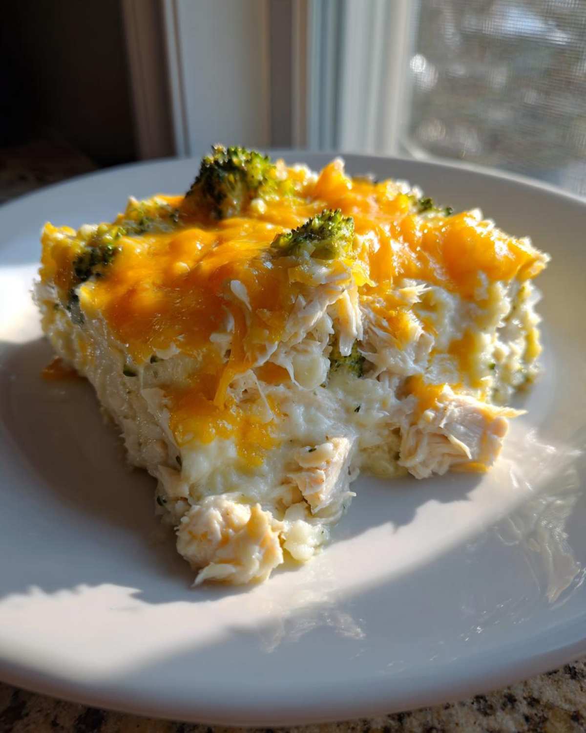 A close-up serving of Dump and Bake Chicken Casserole featuring shredded chicken, creamy sauce, broccoli florets, and melted cheddar cheese.