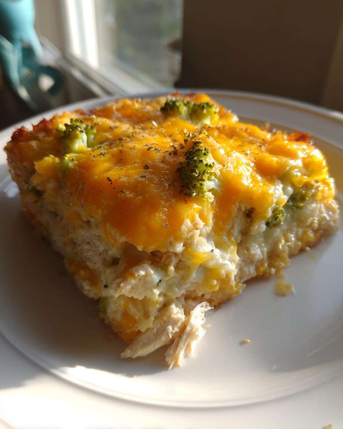 A close-up slice of Dump and Bake Chicken Casserole topped with melted cheddar cheese and broccoli florets.