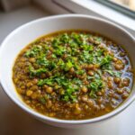 Close-up of a white bowl filled with rich, savory Easy Green Lentil Dal, garnished generously with fresh chopped cilantro.