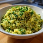 A white bowl filled with bright yellow Easy Lemon Herb Quinoa mixed with fresh chopped parsley.