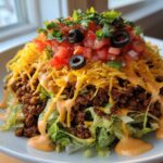 A vibrant, fully loaded taco salad featuring layers of lettuce, seasoned ground beef, shredded cheese, salsa, and creamy dressing.