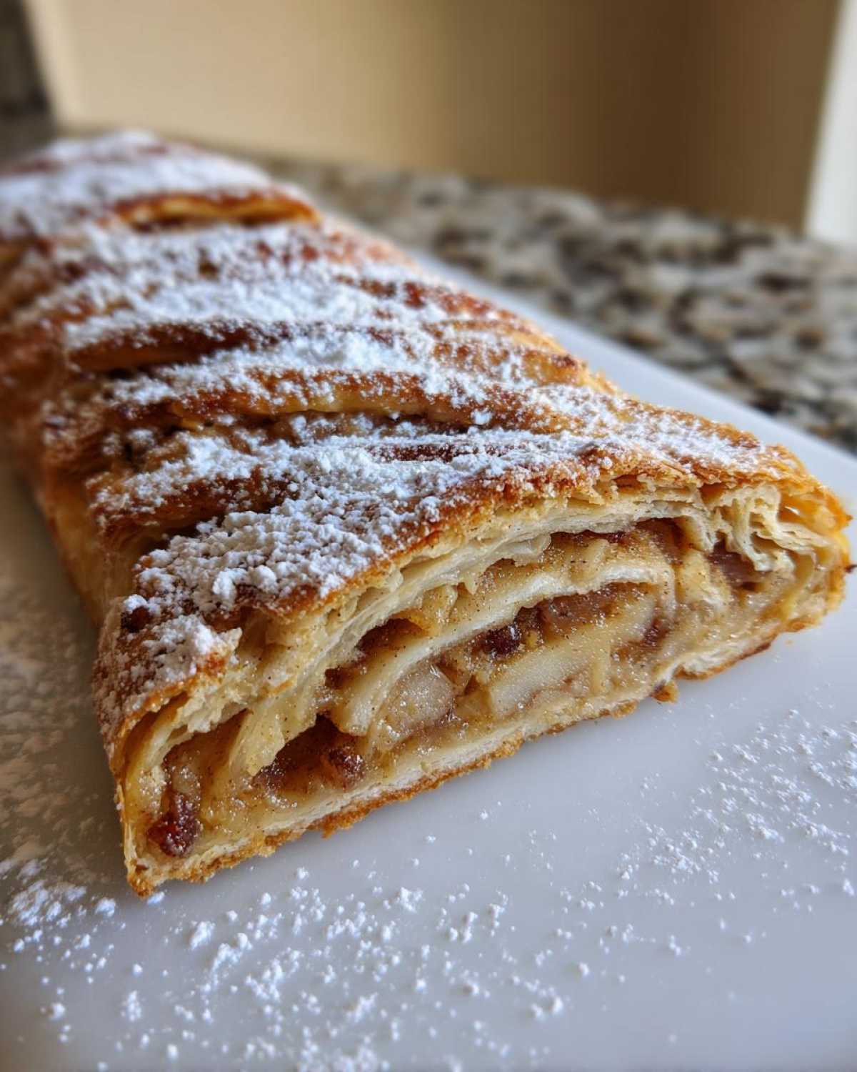 Close-up of a freshly baked apple strudel slice showing flaky pastry layers and apple filling, dusted with powdered sugar.