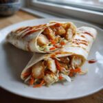 Two halves of Sweet Chili Chicken Wraps filled with glazed chicken pieces and coleslaw, drizzled with extra sauce.