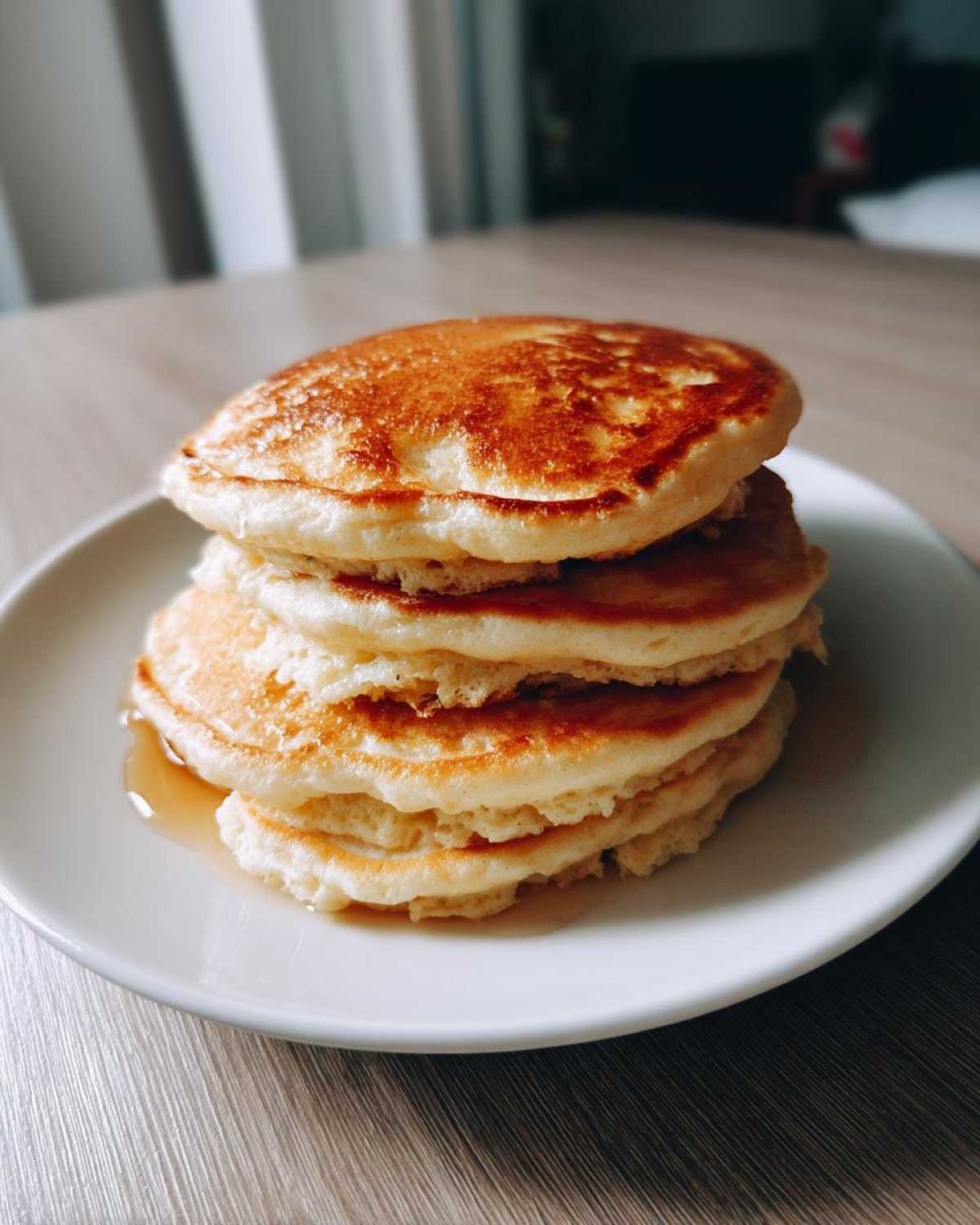 A tall stack of fluffy banana pancakes drizzled with syrup on a white plate.