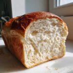 Close-up of a freshly baked japanese milk bread loaf showing its incredibly soft, white, and fluffy interior crumb.