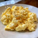 A close-up of fluffy scrambled eggs seasoned generously with black pepper on a white plate.
