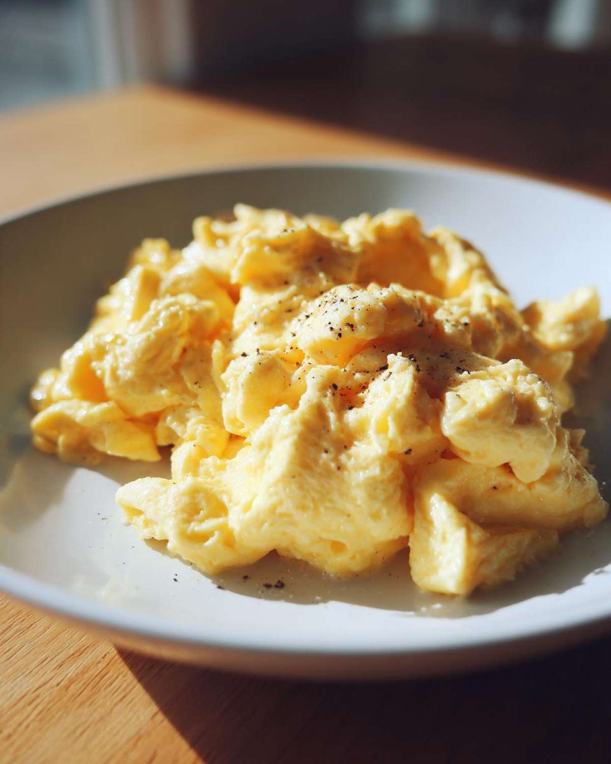 A close-up of perfectly fluffy scrambled eggs seasoned with black pepper, served on a white plate.