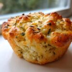 A single, golden brown Focaccia Muffins Recipe item, baked with a bubbly top and sprinkled with dried herbs.