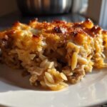 A close-up serving of French Onion Chicken Orzo Casserole with a golden, bubbly cheese crust.