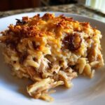 A close-up of a square serving of French Onion Chicken Orzo Casserole showing shredded chicken, orzo pasta, and a deeply browned, cheesy topping.