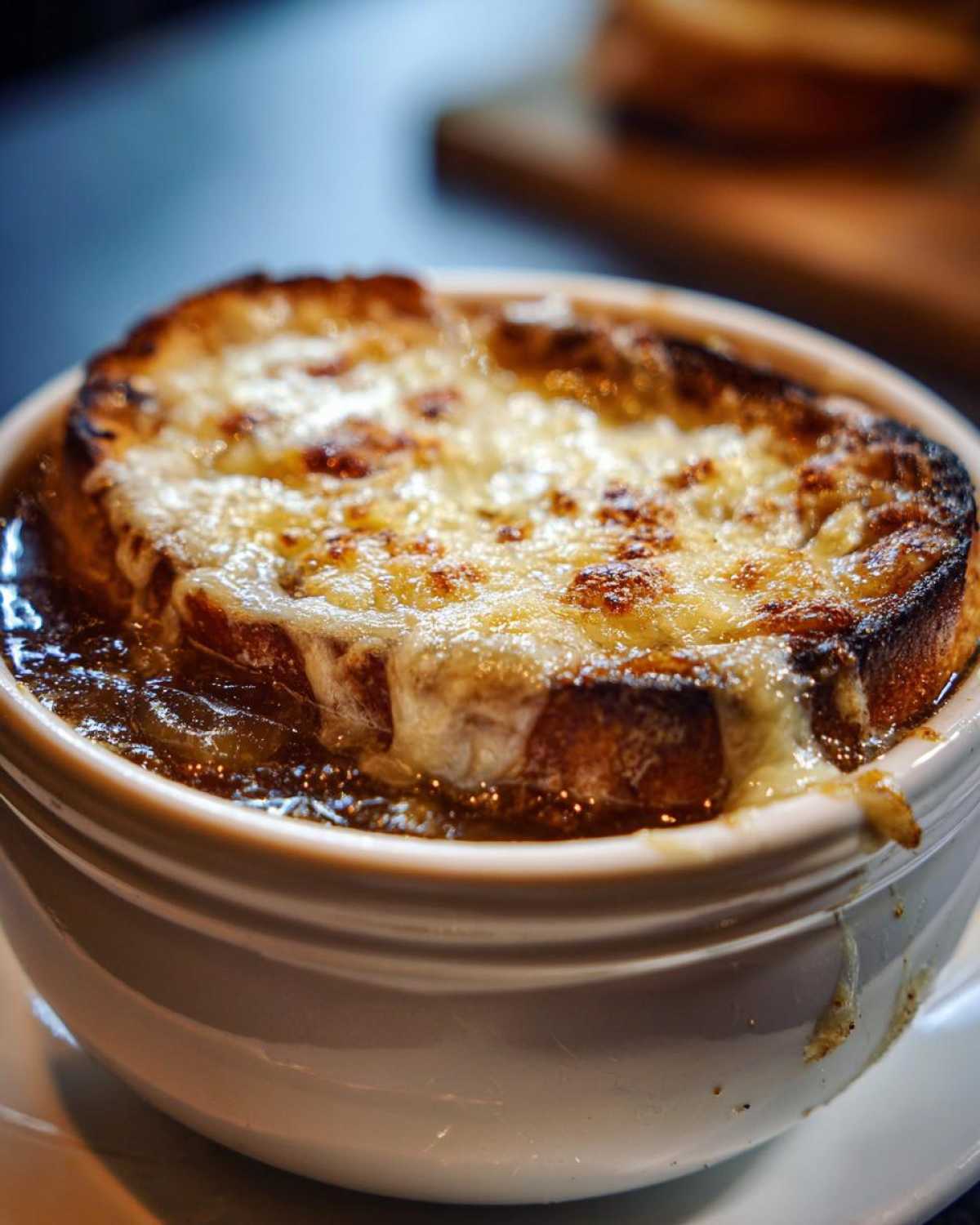 Close-up of a bowl of rich french onion soup topped with a thick layer of melted, browned cheese over crouton.