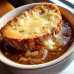Close-up of a bowl of rich french onion soup topped with a thick slice of toasted bread covered in melted, bubbly cheese.
