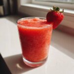 A vibrant, icy strawberry daiquiri served in a clear glass, garnished with a fresh strawberry.