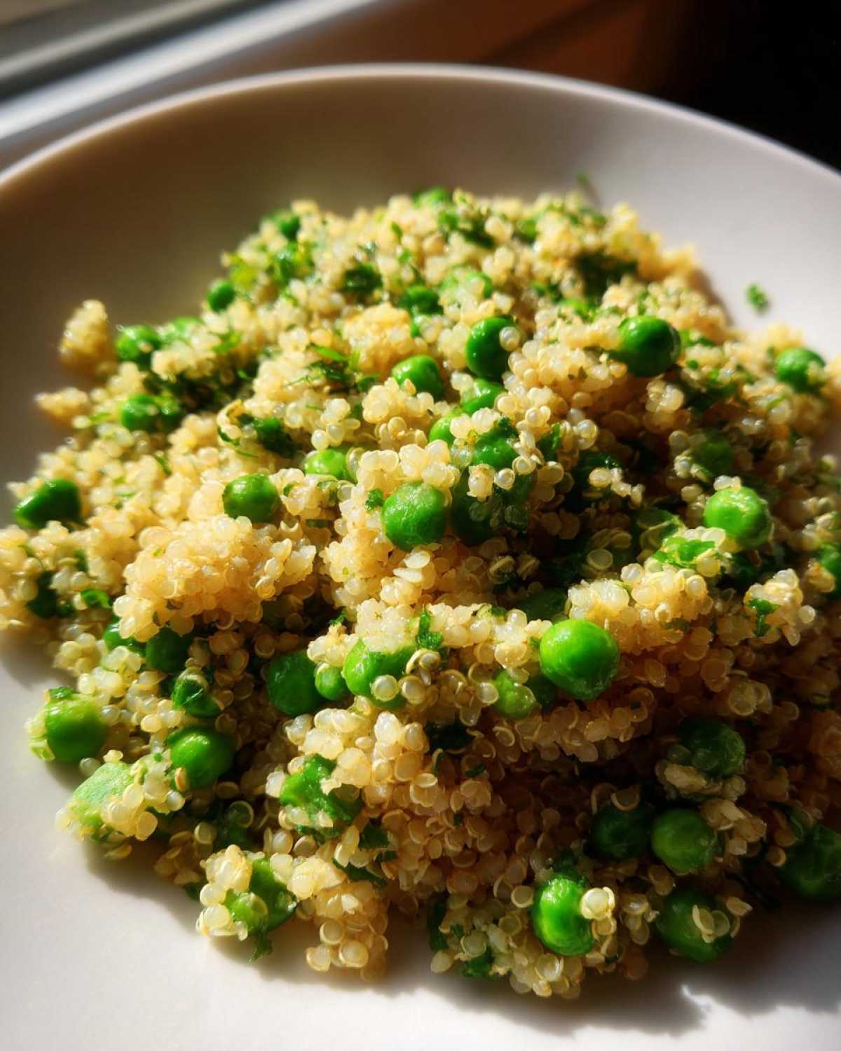 Close-up of fluffy Garlic Butter Quinoa Green Peas mixed with bright green peas and herbs in a white bowl.