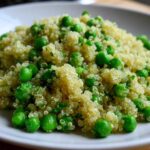 Close-up of fluffy Garlic Butter Quinoa Green Peas mixed with bright green peas and herbs on a white plate.