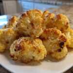 A pile of golden brown, roasted Garlic Butter Roasted Cauliflower florets sprinkled with Parmesan cheese on a white plate.