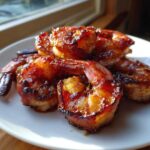 Close-up of several perfectly cooked, glazed bacon wrapped shrimp piled on a white plate.