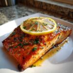 A perfectly cooked piece of glazed baked salmon recipe topped with a fresh lemon slice and chopped parsley.