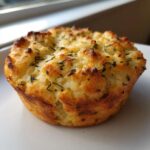 A single, golden brown Focaccia Muffin topped with dried herbs, resting on a white plate.