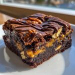 A close-up of a rich, fudgy turtle brownies square topped with pecans, caramel, and a chocolate drizzle.