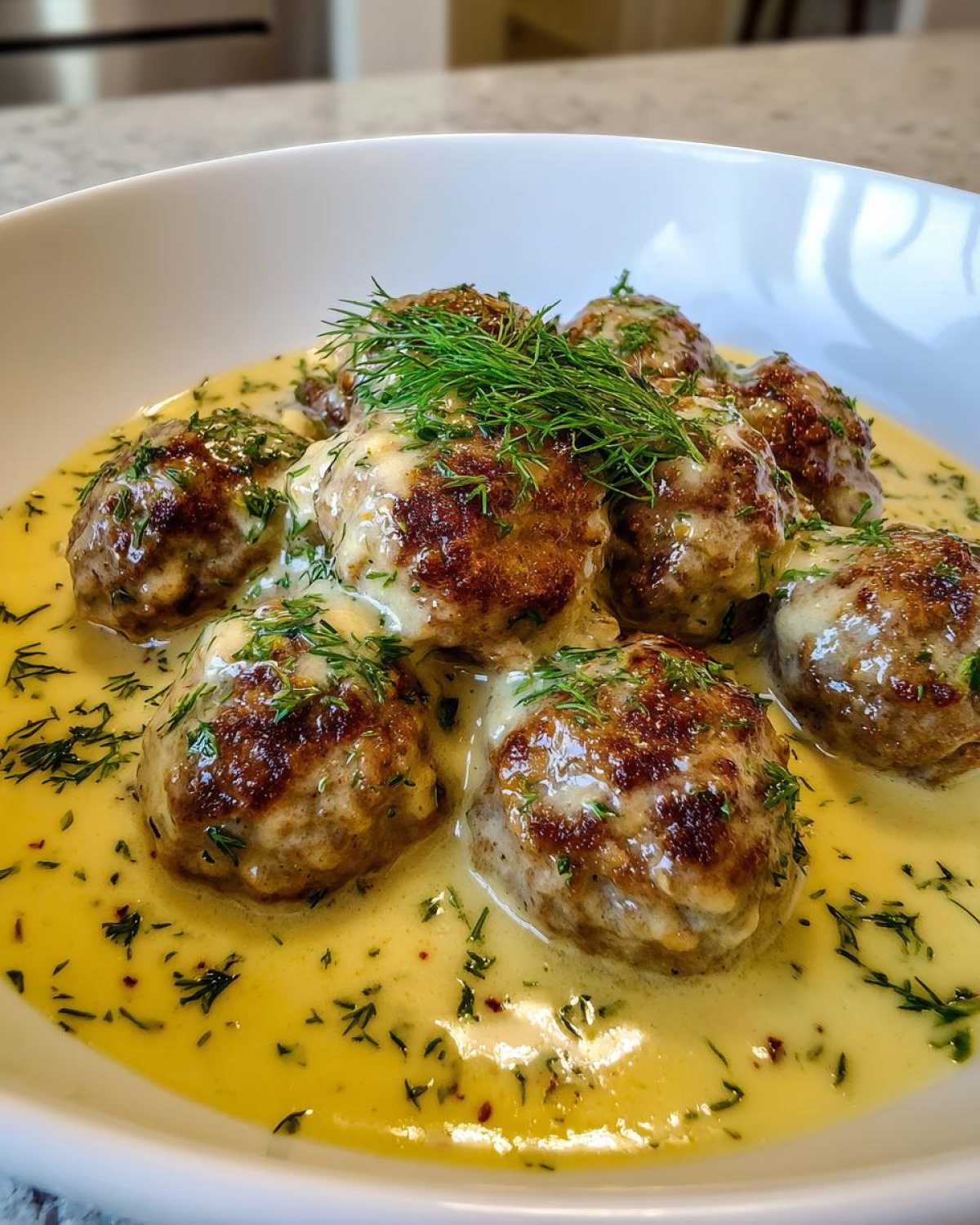 Close-up of browned Greek Meatballs in Lemon Sauce, topped with fresh dill.