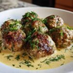 Close-up of six browned Greek Meatballs in Lemon Sauce, generously topped with fresh dill.