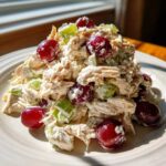 A close-up of a serving of greek yogurt chicken salad mixed with celery and topped with red grapes.