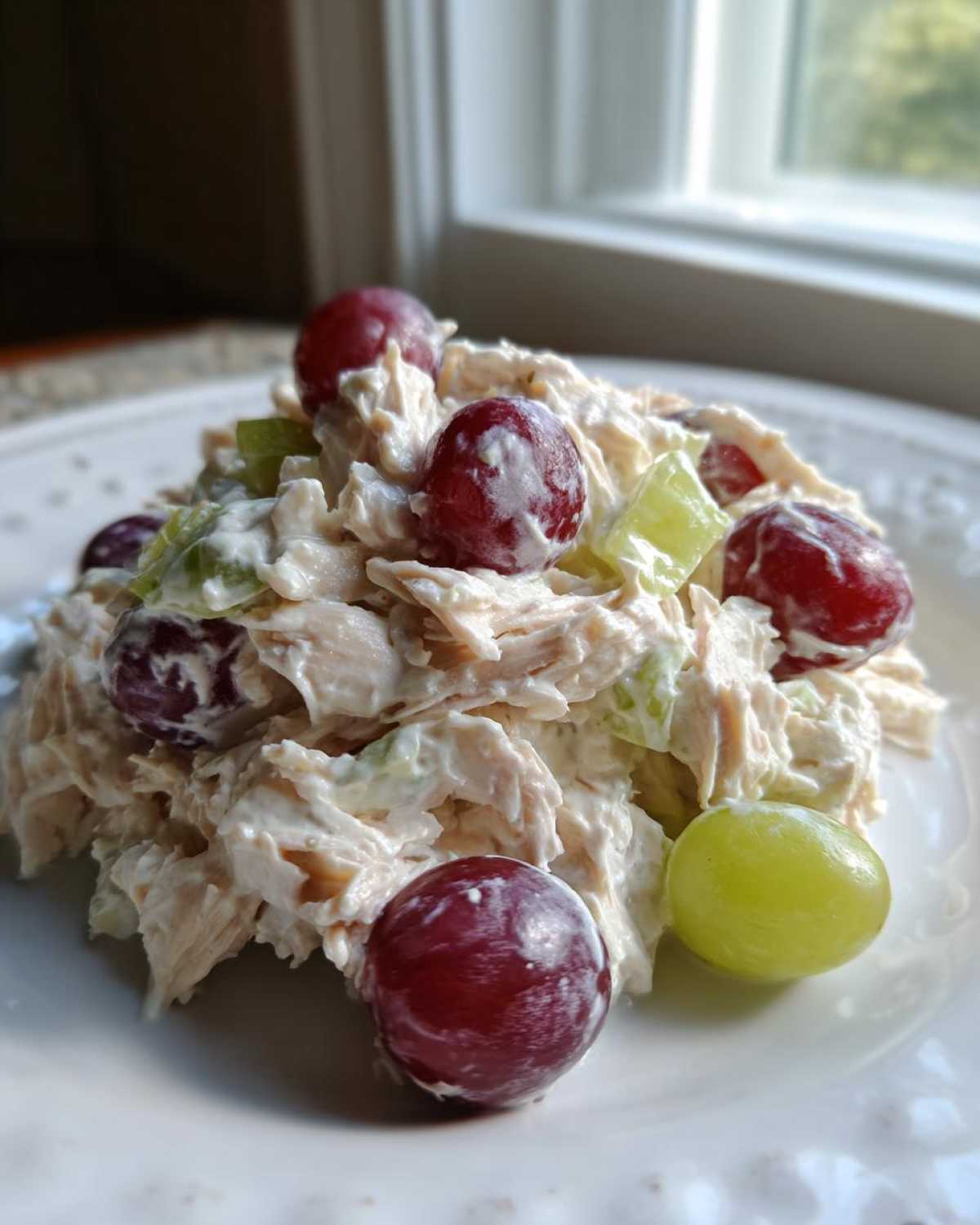Close-up of a scoop of creamy greek yogurt chicken salad mixed with red and green grapes on a white plate.