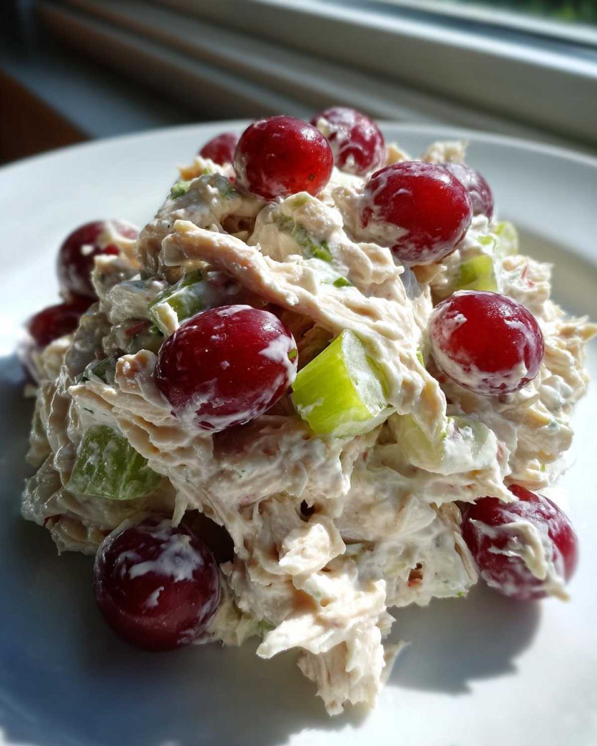 Close-up of a mound of creamy greek yogurt chicken salad topped with bright red grapes and celery chunks.