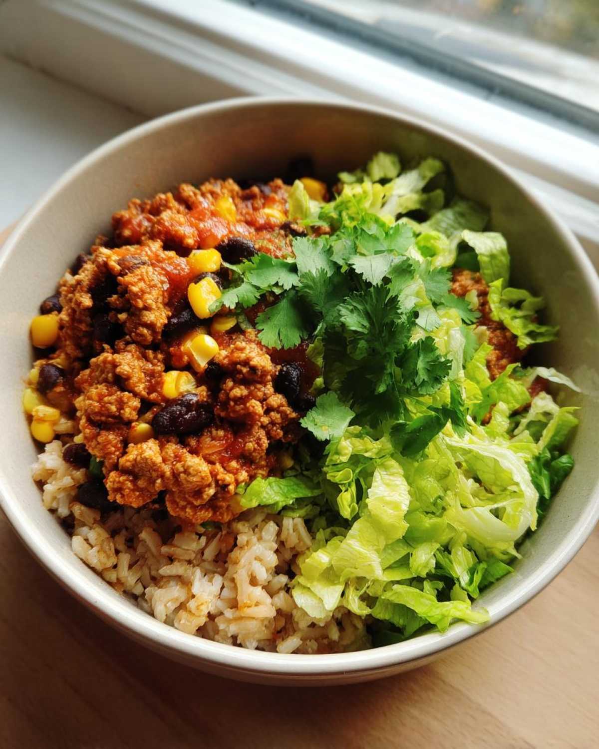 A close-up view of a serving of Ground Turkey Rice Bowls featuring seasoned ground turkey, brown rice, black beans, corn, lettuce, and fresh cilantro.