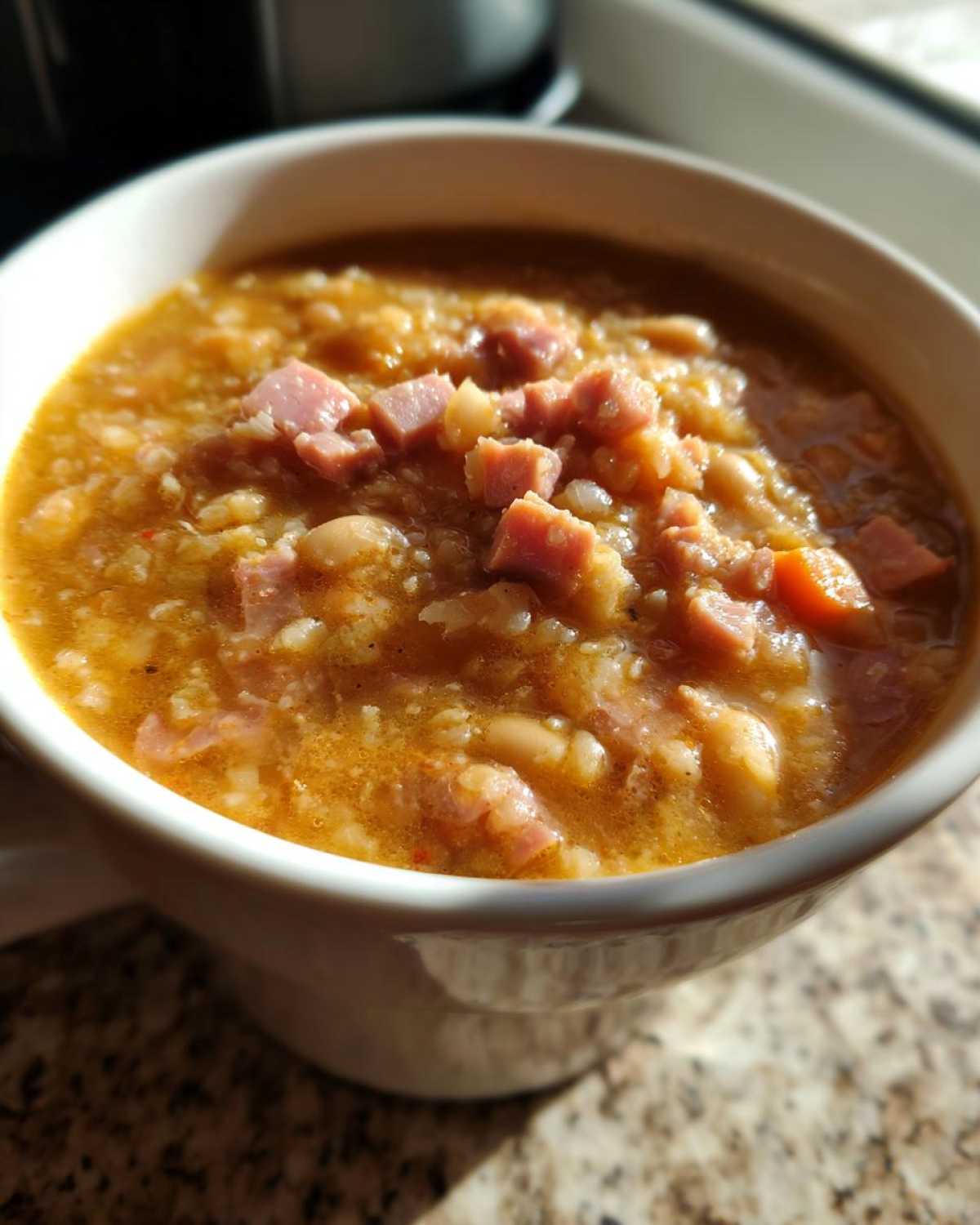 Close-up of a thick, savory bowl of Ham and bean soup topped with diced ham pieces, served in a white mug.